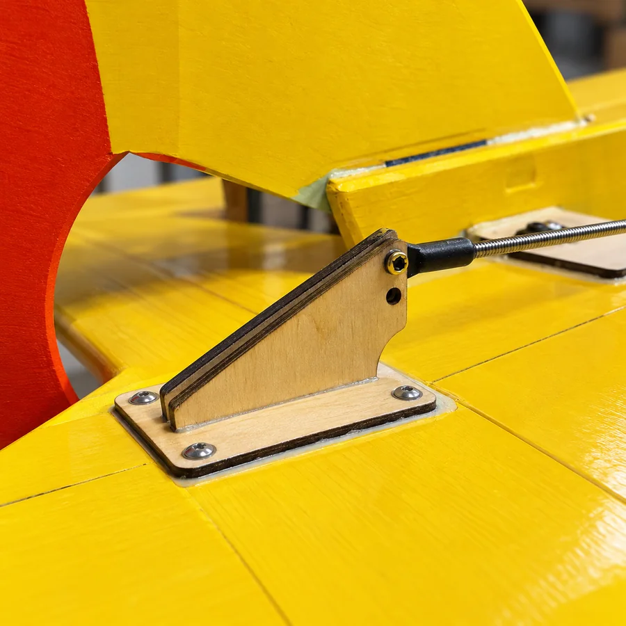 Close-up of the control horn: two laser-cut plywood plates on a base plate held by four countersunk screws, the rod end bolted through the upper hole