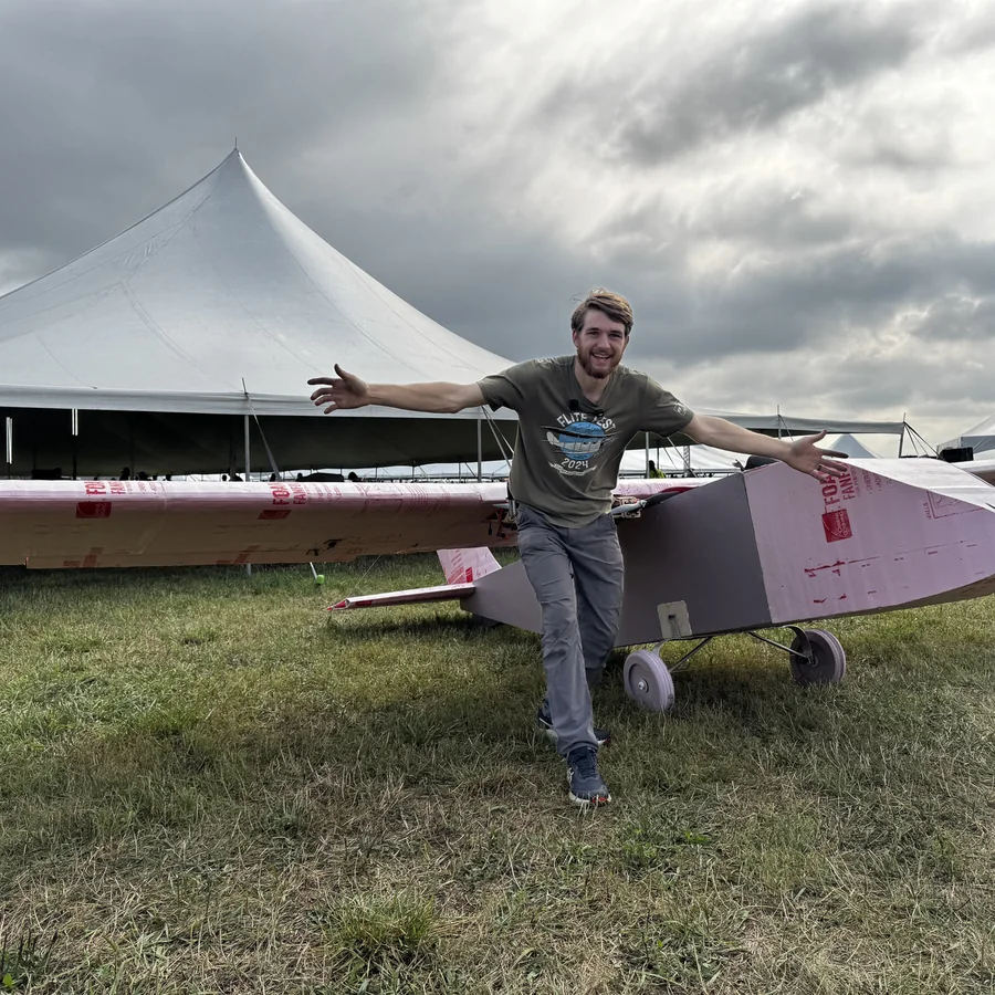 Eric standing arms-out beside the unpainted pink foam 20-foot airplane at Flite Fest